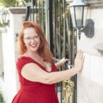 Nikki Lundberg smiling in a red dress beside a decorative gate